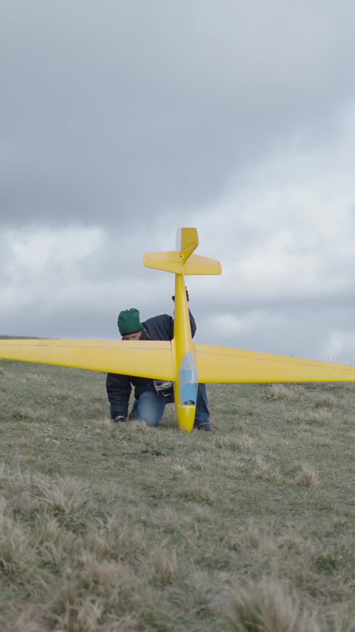 A person with a yellow glider on a grassy hill