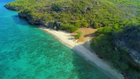 Half-of-San-Juan-beach-Curacao-in-shade-from-tropical-mountain,-drone-rises-tilting-down