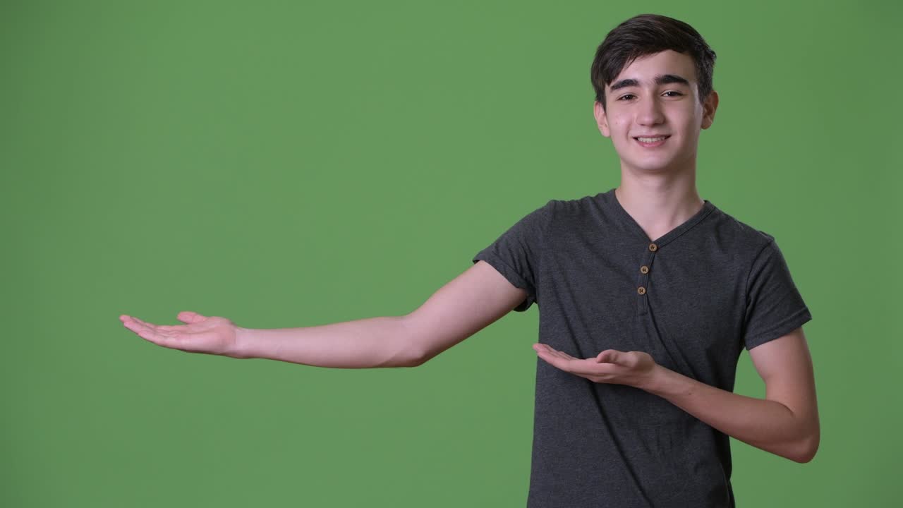 Young handsome Iranian teenage boy against green background