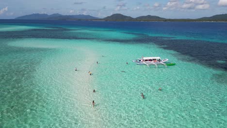 tourists swim in clear blue water of balabac palawan on sand bar by banca boat