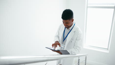 male doctor wearing white coat with digital tablet checking patient notes on stairs in hospital