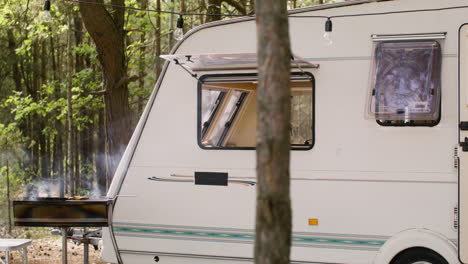 barbecue grilll with smoke and white campervan parked in the forest