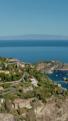 vertical aerial orbit drone shot over the historic town of taormina. buildings at the foot of the rocky mountains in sicily overlooking mediterranean sea cost.