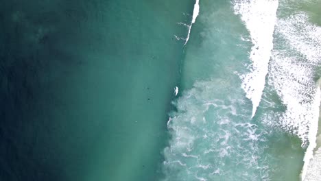 Drohnenaufnahme-Von-Surfern-Von-Oben,-Während-Wellen-An-Einem-Strand-Brechen