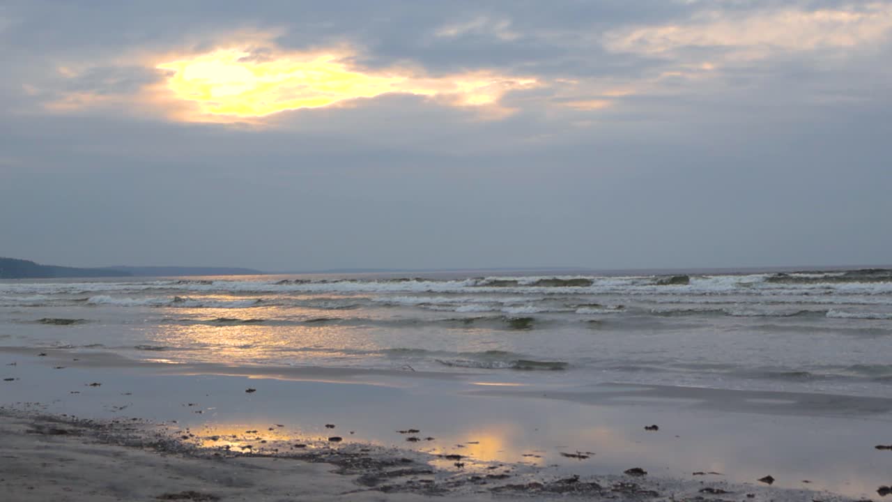 Gorgeous slow motion footage of a beach during sunset or sunrise with waves coming to the sandy cold shoreline in the winter time in slow motion. Sun is reflecting on the sand and ocean sea water wave