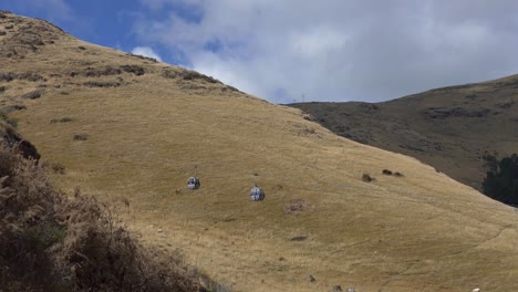 Gondola-cars-pass-in-sun-filled-valley-above-golden-grass-in-summertime---Heathcote-Valley,-Christchurch