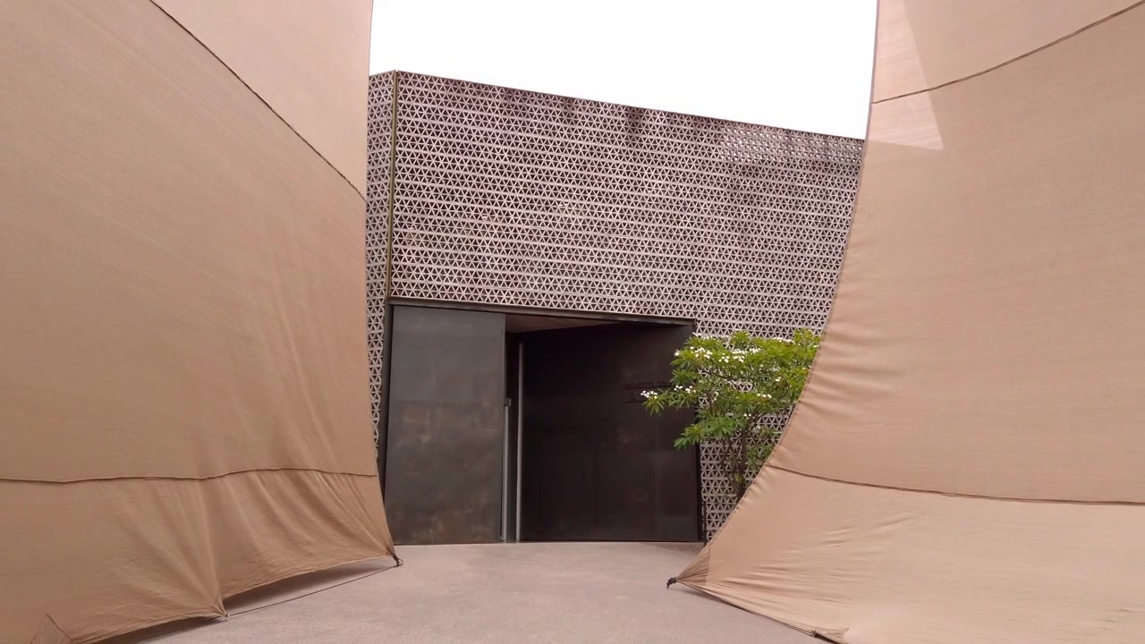 Ground level view of a modern courtyard entrance framed by large fabric canopies, showcasing contemporary architecture, geometric patterns and minimalist design elements