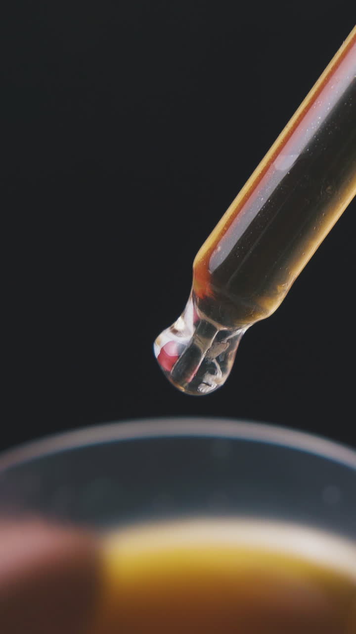 lab assistant takes brown liquid with glass pipette from cup on dark background extreme close view