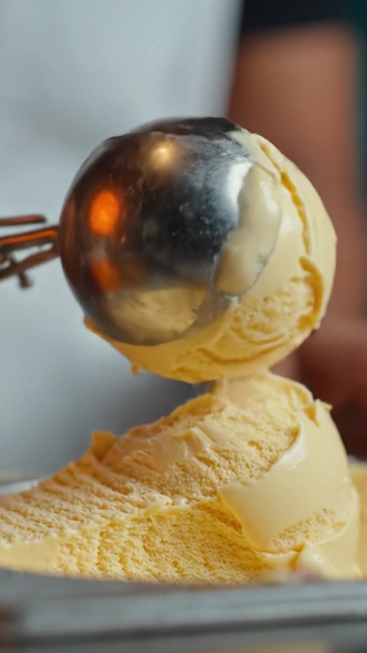 Lækker kugle cremet vaniljeis serveres fra en metalske i lyse og indbydende omgivelser, perfekt til sommernydelse