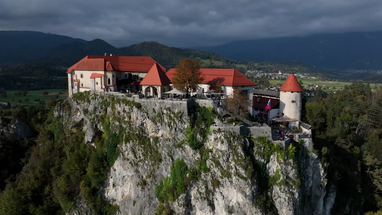 Filmový let dronu nad Bledským jezerem, představující středověký hrad na útesu a ikonický ostrovní kostelík při západu slunce.