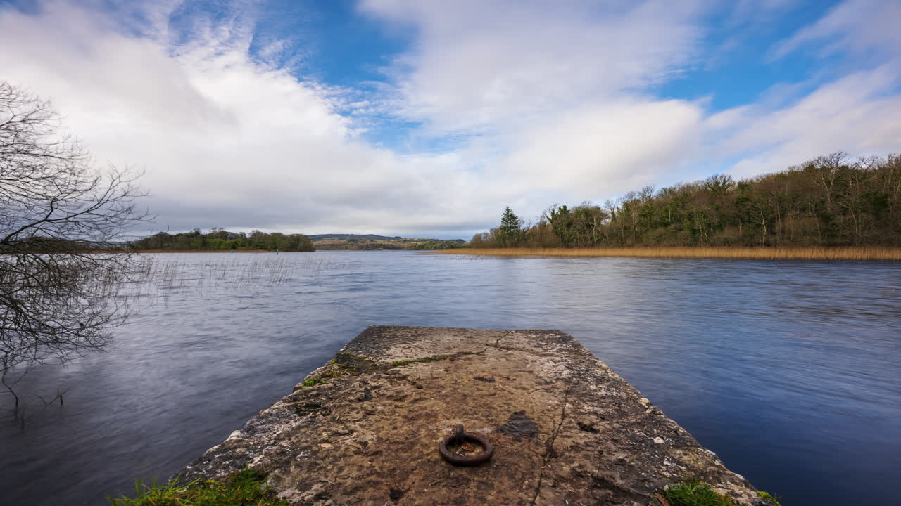 lapso de tiempo de un muelle de lago de hormigón con bosque en la distancia en un día nublado y soleado en lough key en el condado de roscommon en irlanda