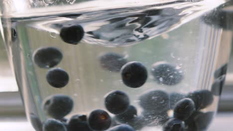 side view of blueberries swirling in glass bowl full of water in slow motion with vortex at top. ripe fruit high in magnesium and fibre. healthy eating food footage