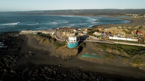 Aerial-orbit-of-pichilemu-beach-at-sunset-with-houses-in-background