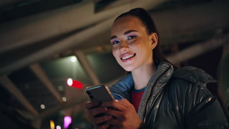 Lächelndes-Mädchen,-Das-Abends-In-Der-Stadt-Auf-Das-Smartphone-Blickt,-Nahaufnahme.-Frau-Durchsucht-Inhalte