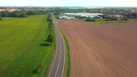 Aerial-view-of-crop-field-blowing-in-the-wind-with-road-winding-through-it-and-small-city-in-the-background