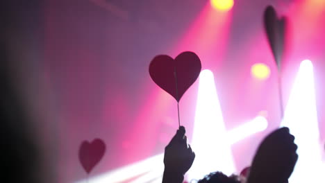 concertgoers waving heart shaped cards, expressing deep emotional connection and passionate support during live music performance, radiating collective love and enthusiasm