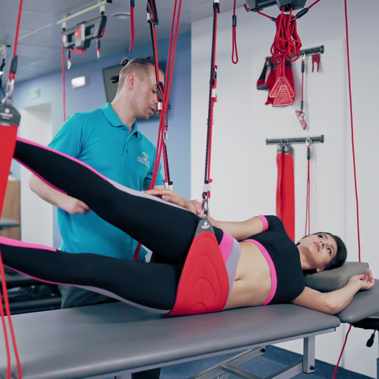 Professional instuctor helps the patient doing recovery exercises in modern rehab gym. Personal trainer shows the client how to do workout with suspension ropes to relieve pain after the injury.