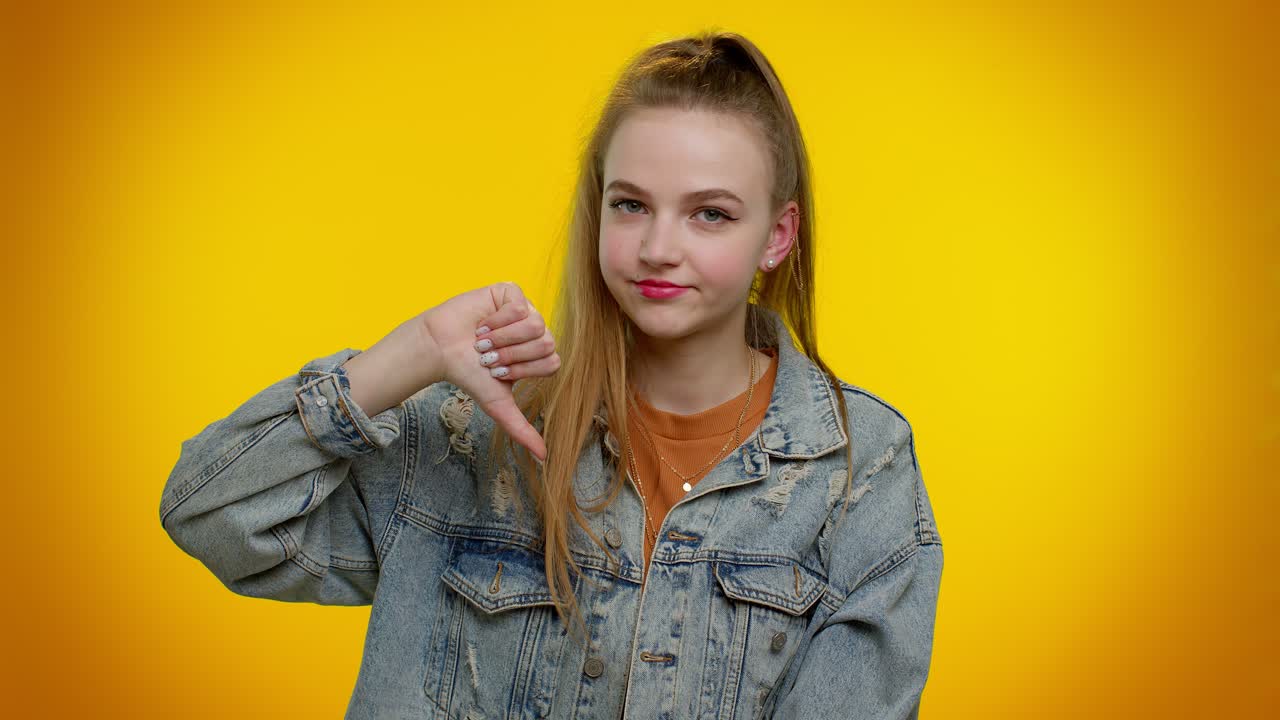 Upset girl in denim jacket showing thumbs down sign gesture, disapproval, dissatisfied, dislike