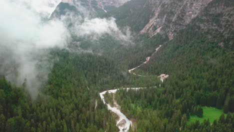 Dolly,-Nach-Unten-Geneigte-Drohnenaufnahme-Der-Alpen-Mit-Niedrigen-Wolken,-Die-über-Einem-Fluss-Fliegen