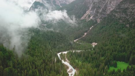 dolly, tilt down drone shot of the alps with low clouds flying above a river