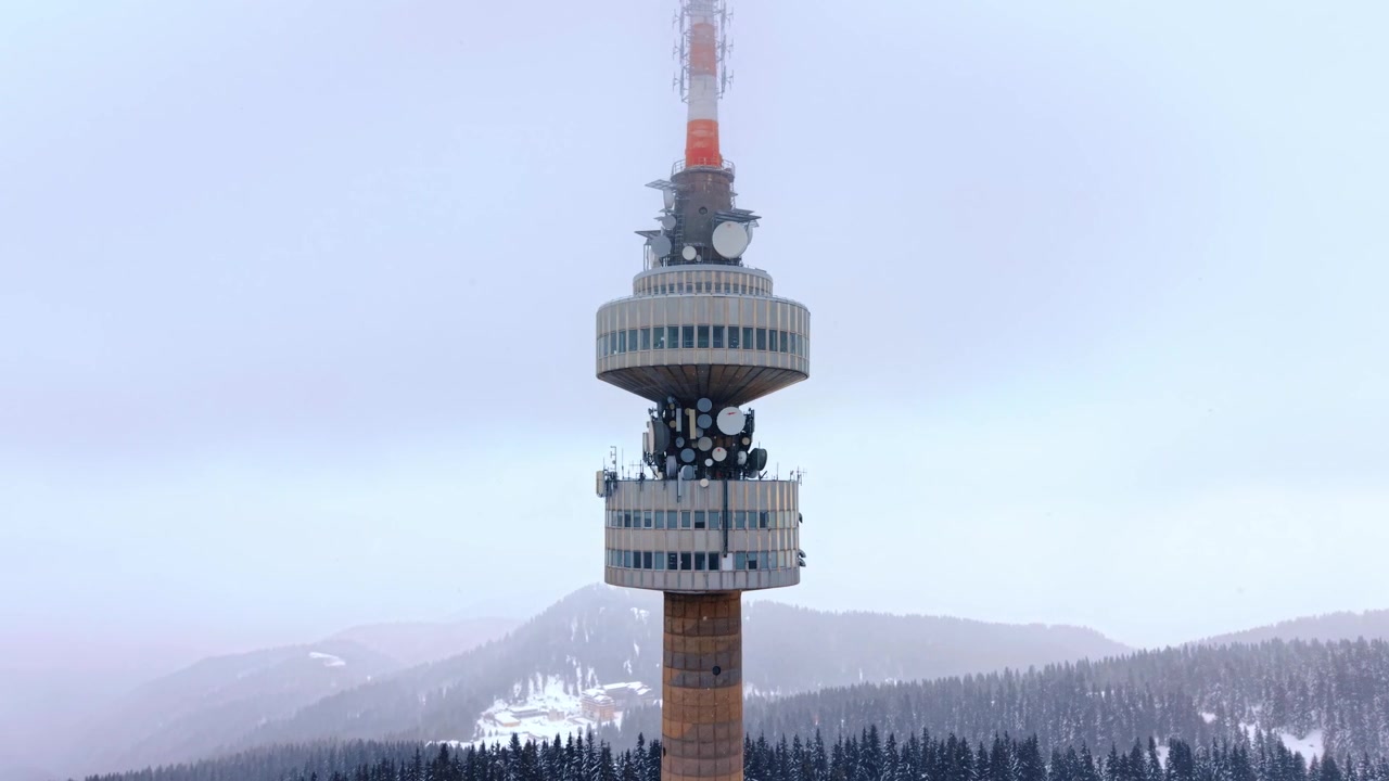 Vista di una torre montana in inverno. Un'alta torre di comunicazione si erge in un paesaggio innevato con pini e montagne sullo sfondo durante l'inverno.