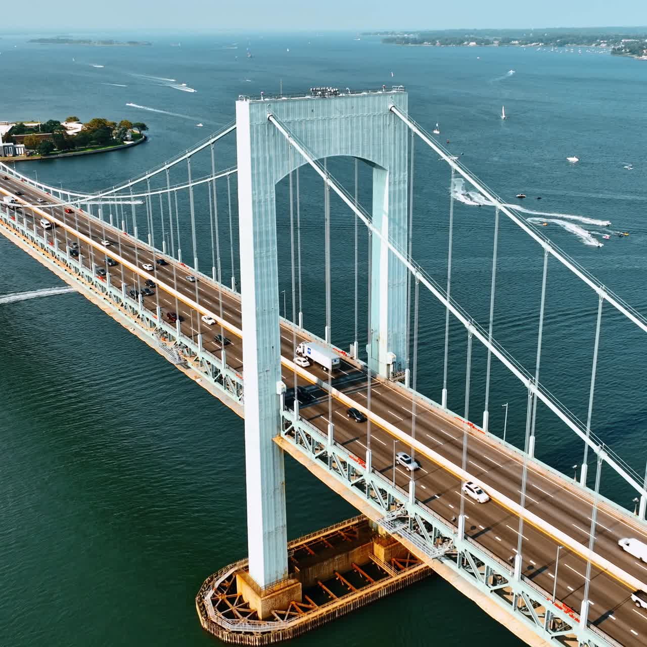 Traffic on the roads of the Throgs Neck Bridge. Multiple yachts and boat are on the East River. Top view