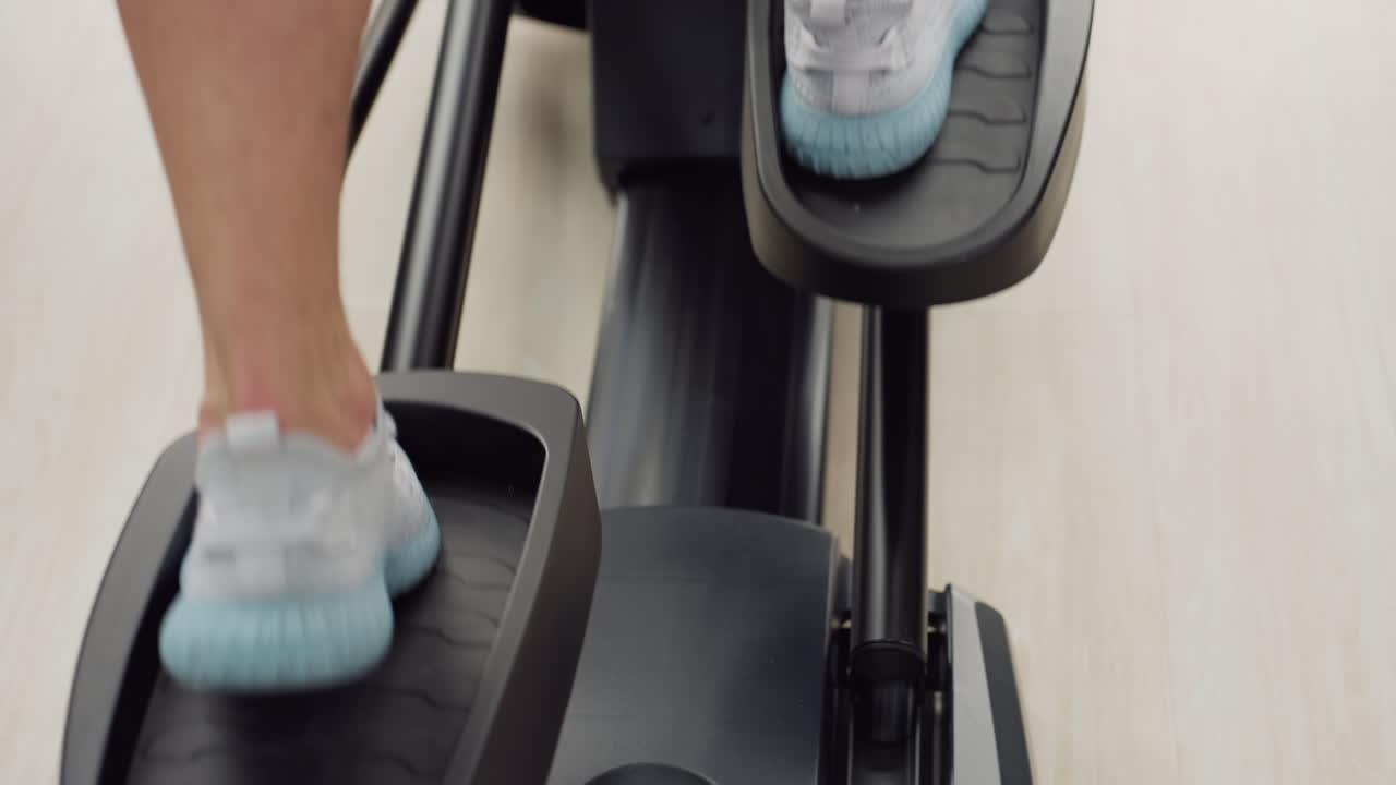 Leg view of white man wearing sports sneakers powering elliptical trainer in bright modern gym near panoramic windows dynamic stride showcases athletic movement cardio intensity strength