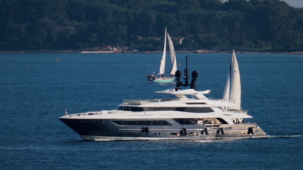A white boat moving on the sea with other small boats and trees on the background in the French Riviera