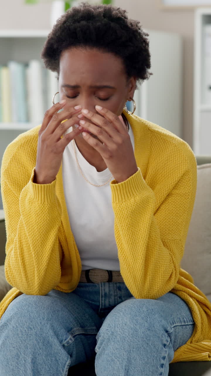 A young woman sits in a chair with her head in her hands, looking sad and distressed.