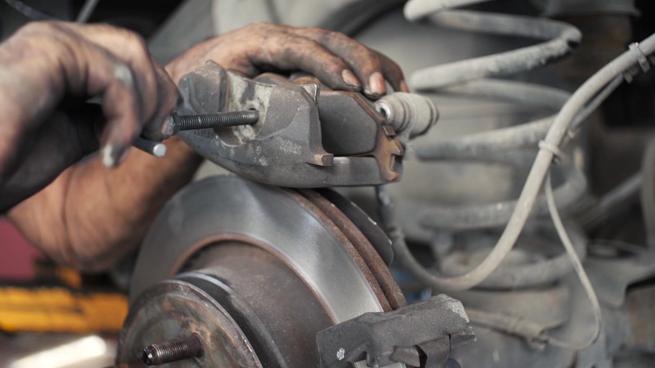 Latin American Car Mechanic With Dirty Hands Using Economic Tools To Replace Brake Pads and Disk. Mexican Car Fix Garage, Close Up To Brakes In Slow Motion