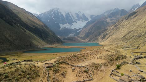 an aerial flyover soars above ancient ruins and a remote campsite, revealing the stunning turquoise glacial lakes at the base of the huayhuash mountains in peru