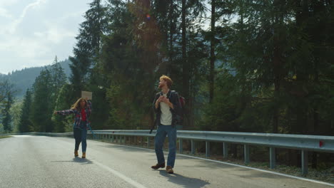 backpackers standing mountain road outdoors. hitchhikers wave hands on holiday.