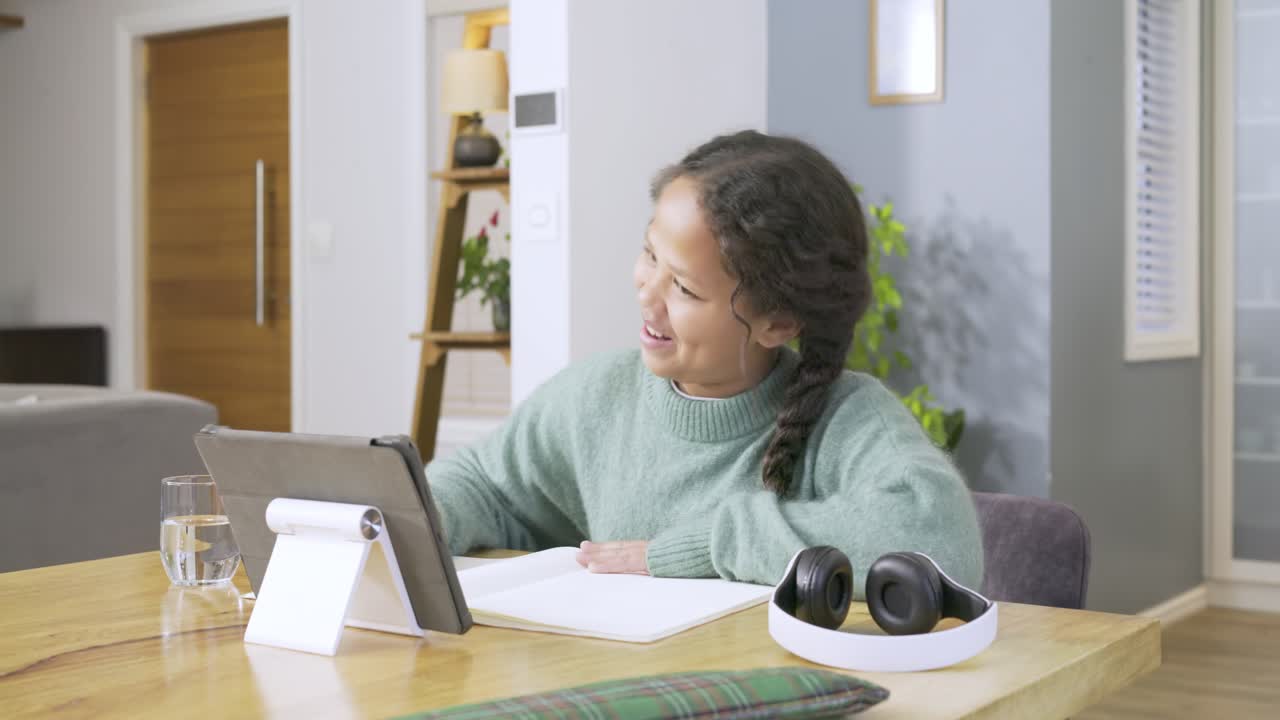 Girl pulling headphones, bopping head then writing notes and cheering at tablet at dining table