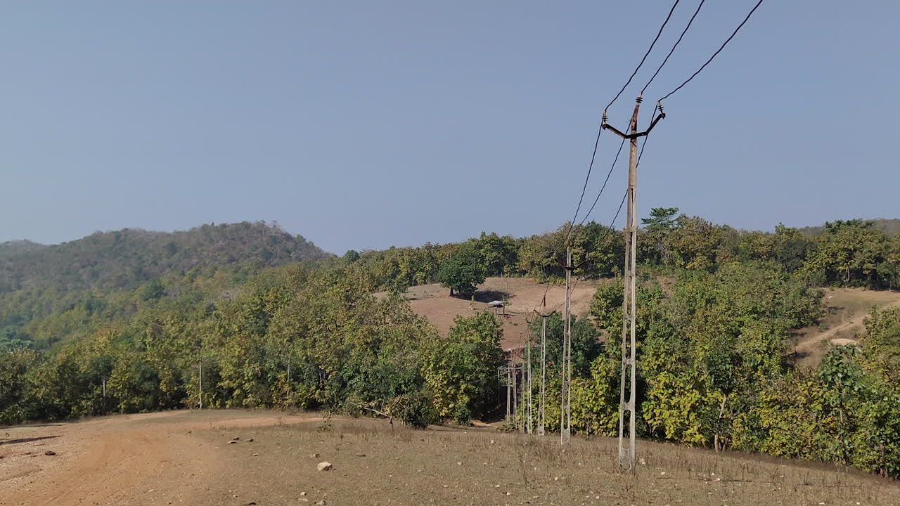 un zoom suave revela el paisaje ondulado de la india, acentuado por una línea de postes telefónicos o líneas eléctricas