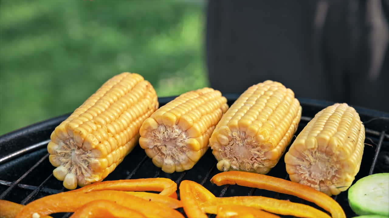 Frying vegetables on a grill at glamping. Corn cobs, bell peppers, onions, zucchinis. Man greases vegetables with oil