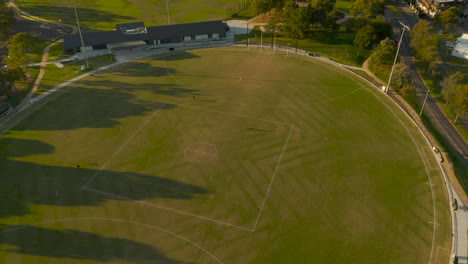 friends practicing kicking australian rules football on football oval