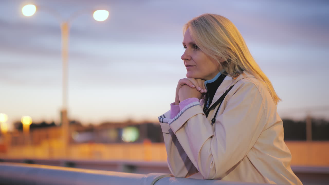 una mujer de mediana edad se para en un puente en la barandilla y mira pensativamente a lo lejos en un