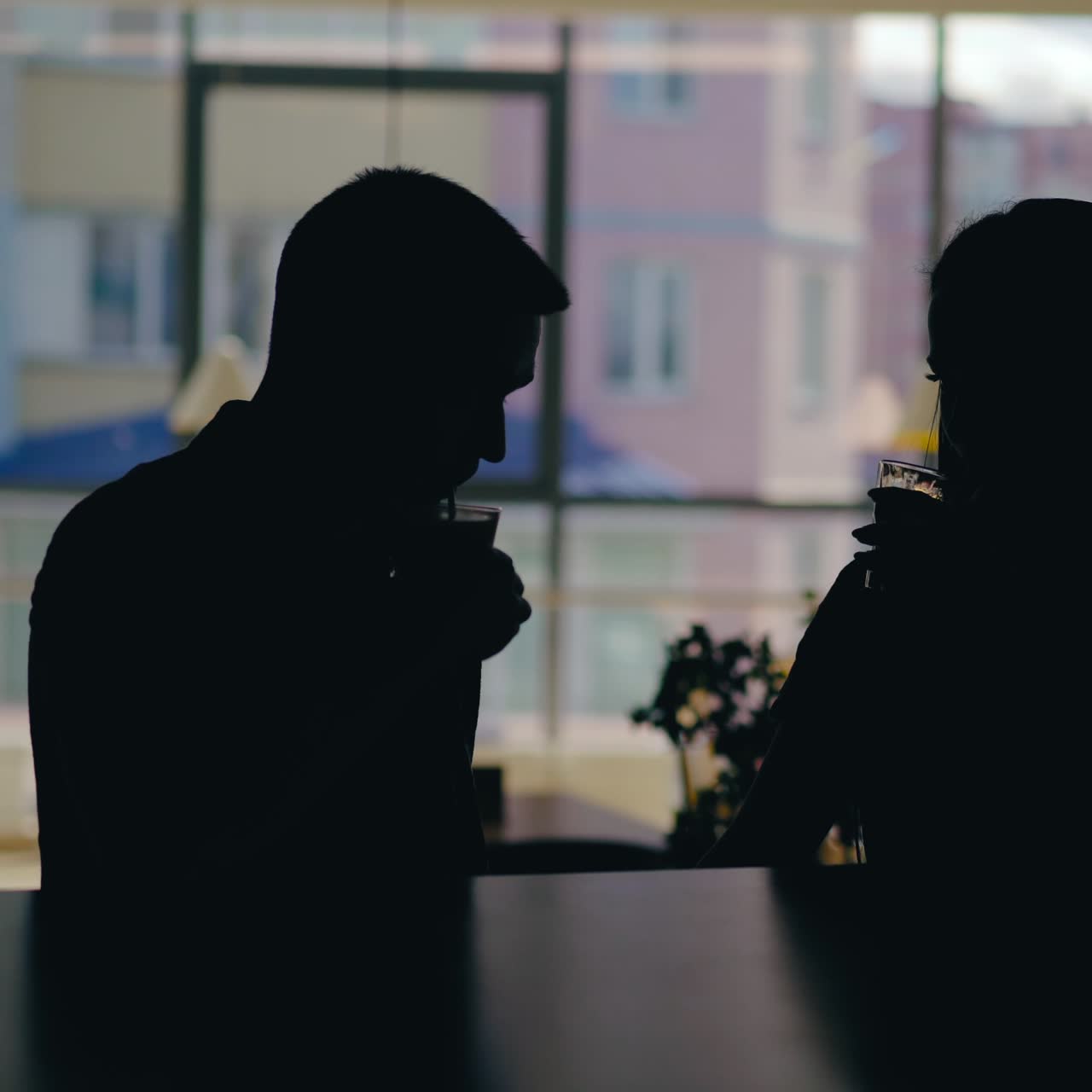 silhouettes of man and woman are talking at a table in the cafe and drinking drinks on the background of the window. Blurred background