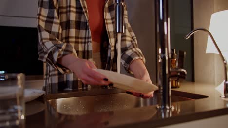 close-up shot of a happy and cheerful girl in a checkered shirt listening to music on wireless red headphones and washing dishes in the kitchen in a modern apartment in the evening