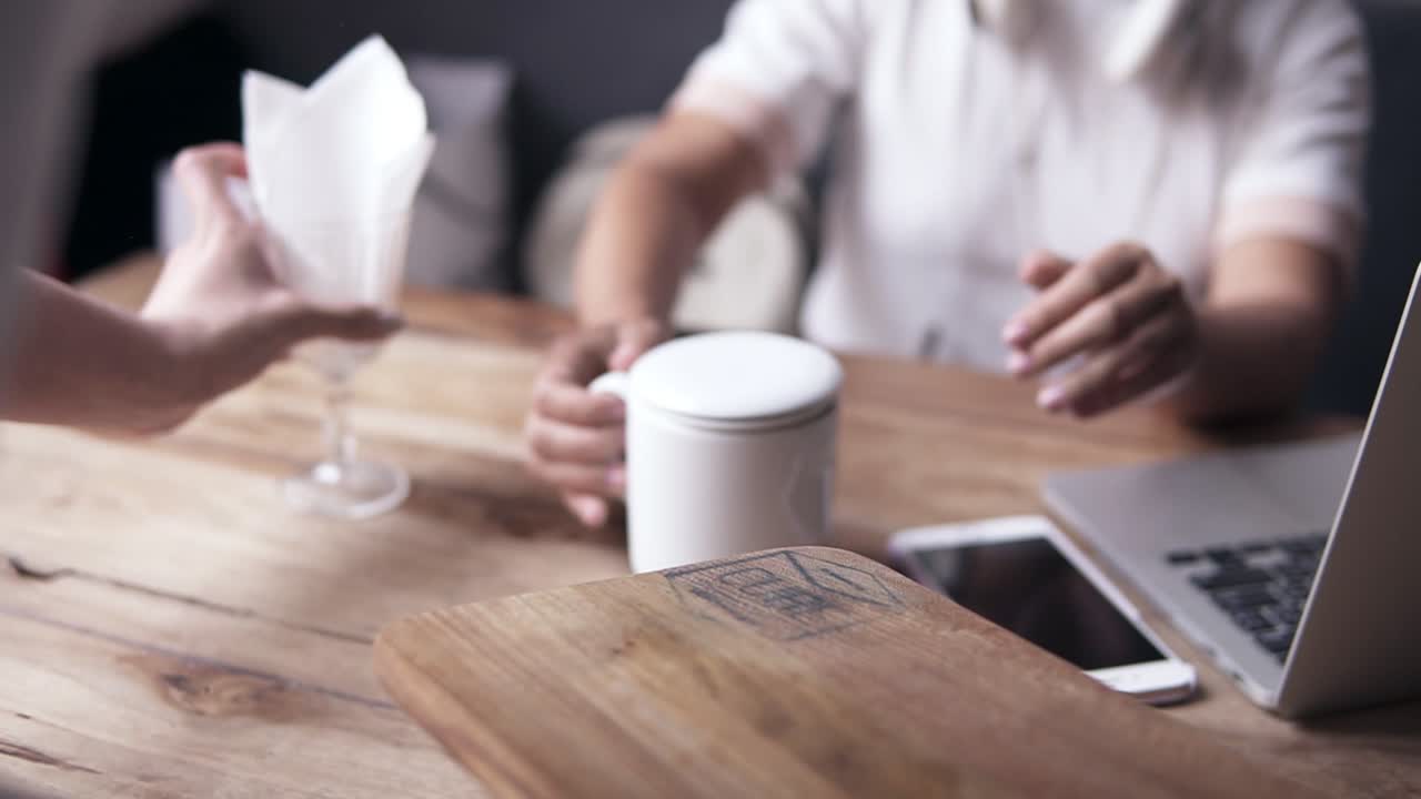 hermosa mujer joven de blanco, sentada en una cafetería en un sofá azul, la camarera trae una taza de té y la pone en la mesa. hay computadora portátil y móvil en la mesa. auriculares blancos en el cuello