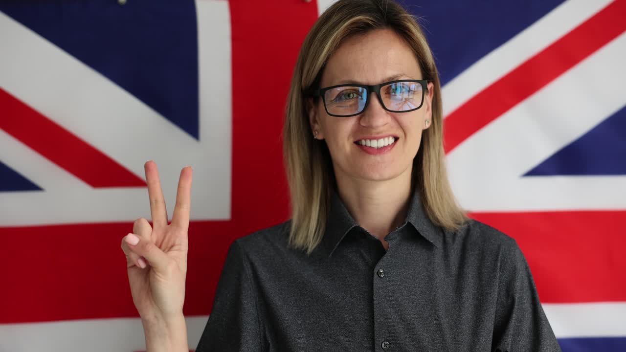 Profesor con gafas hace el signo de la victoria frente a la bandera británica