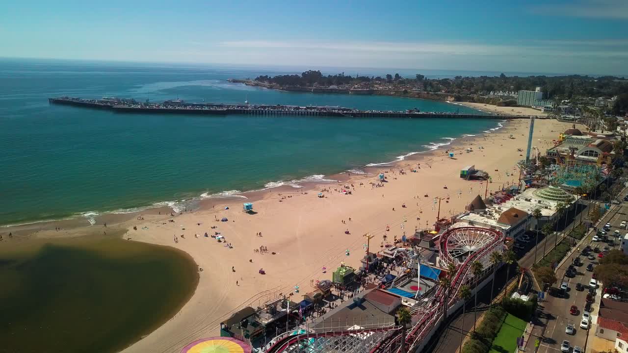 Aerial flyover beach boardwalk amusement park towards ocean. 4K
