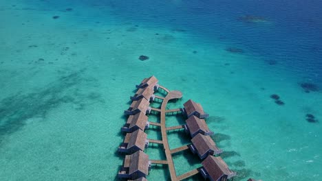 las cabañas tipo bungalow sobre el agua en la playa de maldivas dan belleza a las aguas poco profundas de color azul claro y al agua azul profunda: toma aérea