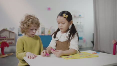 little girl and little boy playing with alphabet puzzle in montessori school