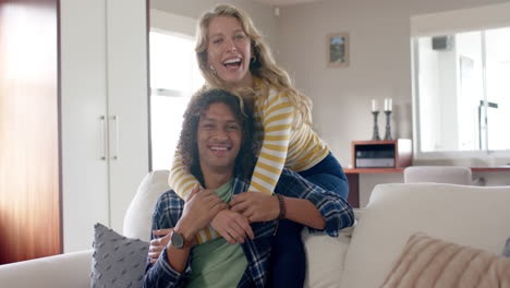 portrait of happy diverse couple embracing and sitting on couch in living room, slow motion