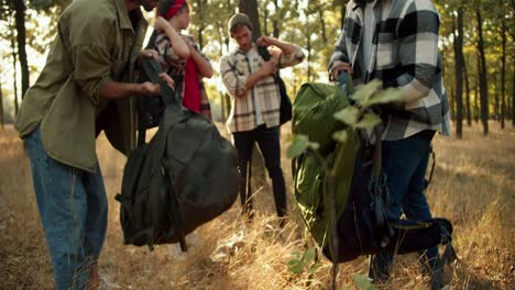 a group of people in special hiking clothes pick up their hiking backpacks and begin to move through the sunny summer forest. the end of the camping trip and the beginning of a new path