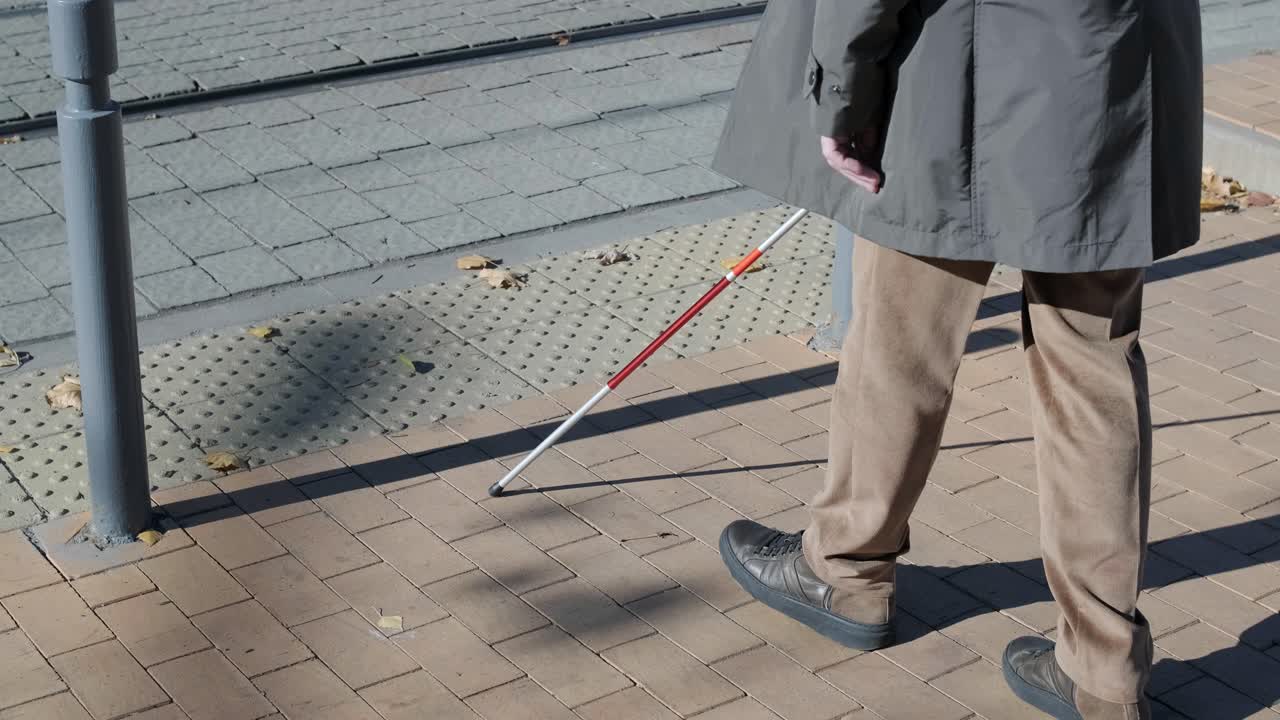 Visually impaired man crossing the road with his stick with the help of tactile pedestrian sidewalk for the visually impaired in the city.