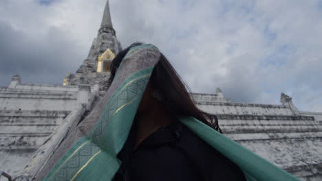 woman covering her face in the buddhist temple wat arun, temple of dawn, holding a scarf, which is located on the banks of the chao phraya river