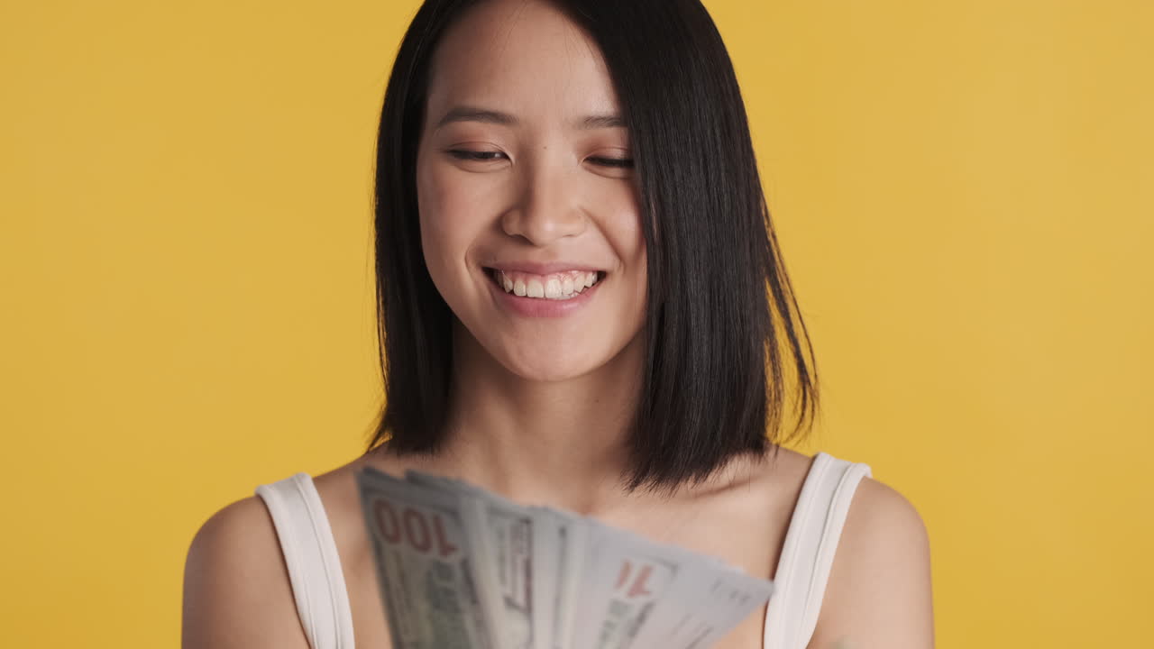 Asian woman looking happy while holding money on camera.