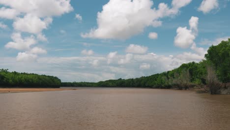 hyperlapse shot from a small boat sailing on the muddy tropical river in africa with beautiful clouds, blue sky and fresh green trees on hot summer day